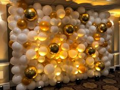 a large balloon wall is decorated with gold and white balloons