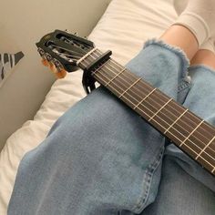 a person sitting on a bed with a guitar in their lap