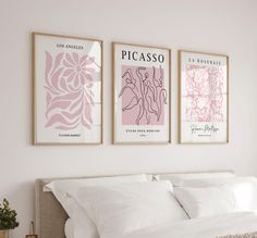 three posters on the wall above a bed in a room with white sheets and pillows