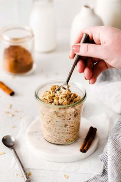 a person is spooning into a jar of oatmeal with cinnamon sticks