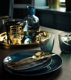 the table is set with gold and black plates, silverware, and glass cups