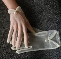 a woman's hand with white gloves and pearls on it