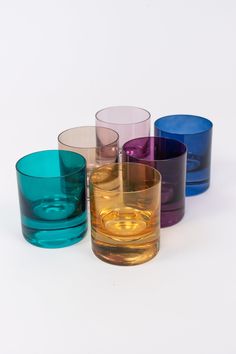 four different colored glasses sitting next to each other on a white surface, with one empty glass in the middle