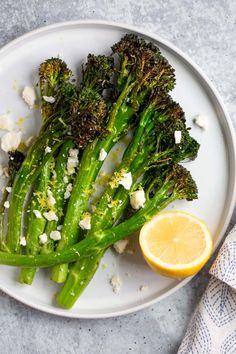 broccoli with feta cheese and lemon on a white plate next to a napkin