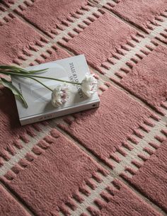 a book with some flowers on it laying on the floor next to a rug that is pink and white