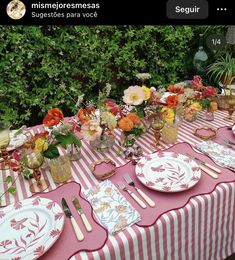 the table is set with plates, silverware and flowers on pink striped cloths