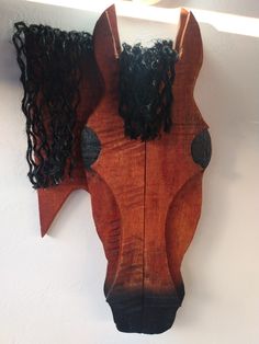 a wooden horse head mounted to the wall with long hair on it's face