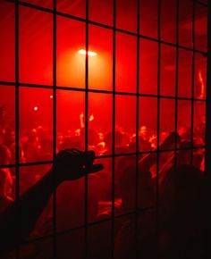 a person's hand reaching out through the bars of a jail cell at night