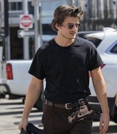 a man in black shirt and brown pants walking down the street with his handbag