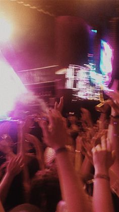 a crowd of people at a concert with their hands in the air and lights on