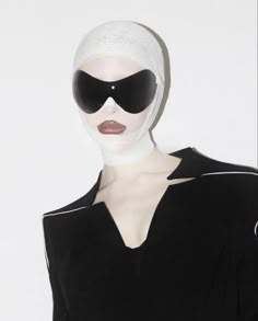 a woman with white hair and sunglasses on her head wearing a black dress, standing in front of a white wall