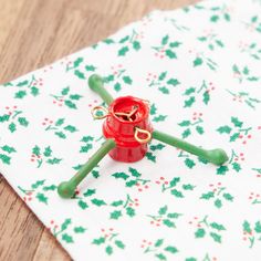 a small red object sitting on top of a white cloth covered in green and red flowers