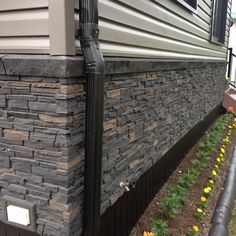 the side of a house with flowers growing in front of it and a gutter hose attached to the wall