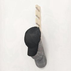 a hat hanging on the back of a wooden coat rack, with a black baseball cap attached to it