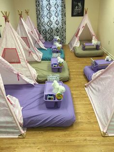 a room filled with lots of beds covered in pink and purple tents next to a window