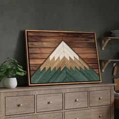 a painting on the wall above a dresser with drawers and a potted plant next to it