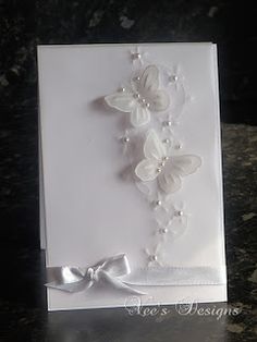 a white greeting card with butterflies and pearls on it's side, attached to a silver ribbon