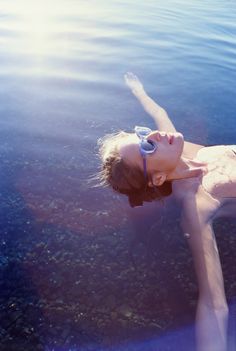 a woman is floating in the water with her legs spread out and wearing goggles