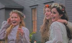 three women dressed in period clothing laughing and posing for the camera with candles behind them