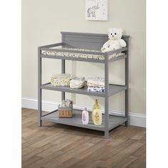 a baby crib with a teddy bear on top and diapers in the bottom shelf