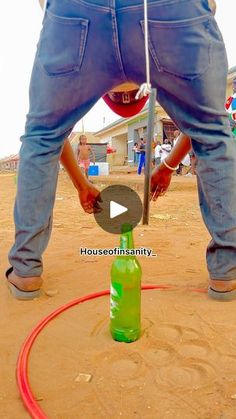 a man standing over a green bottle on top of a red hose in the sand