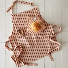 an apron with a bagel on it sitting on a tile floor next to a spoon