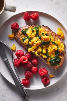 a white plate topped with toast and raspberries next to a cup of coffee