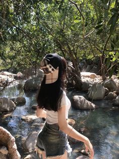 a woman is standing on rocks in the middle of a stream wearing a hat and shorts