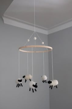 three sheep hanging from a circular wooden chandelier in a room with gray walls