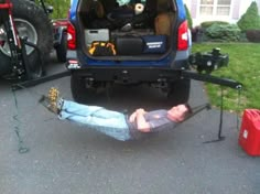 a man laying on the ground in front of a blue truck with its trunk open