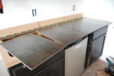 an unfinished kitchen counter is being built with black cabinets and silver appliances in the background