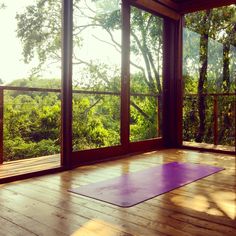 a yoga mat is in the middle of a room with large windows looking out on trees