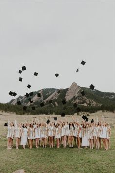 a group of people standing on top of a grass covered field with graduation caps in the air