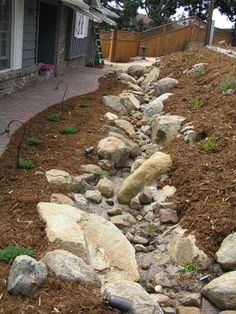 a rock lined path in front of a house next to a yard with grass and rocks