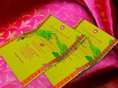 two yellow and red wedding cards sitting on top of a pink cloth