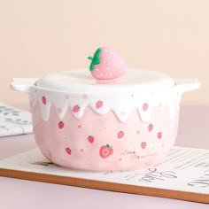 a pink and white ceramic bowl with a strawberry on top, sitting on a table