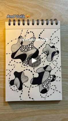 a spiral notebook with black and white drawings on it, sitting on a wooden surface