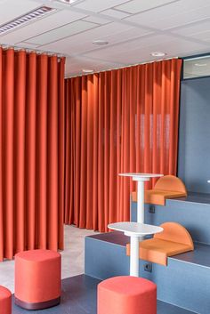 an orange and blue room with some stools in front of red curtains on the wall