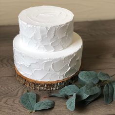 a three tiered white cake sitting on top of a wooden table next to leaves