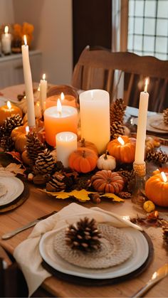 a dining room table with candles, plates and pine cones