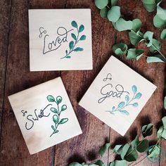 three wooden coasters with embroidered words on them and green leaves scattered around the edges