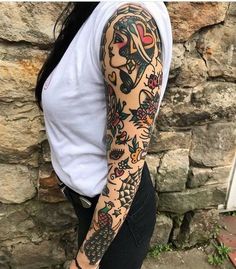 a woman with a tattoo on her arm next to a stone wall holding a cell phone