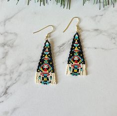 a pair of beaded earrings on top of a marble counter with pine branches in the background