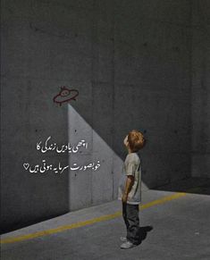 a young boy standing in an empty parking lot with graffiti on the wall behind him