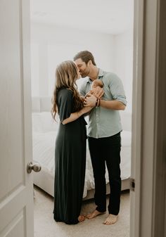 a man and woman kissing while standing in front of a bed with their baby boy