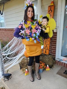 a woman holding a baby in her arms while standing next to a house decorated for halloween