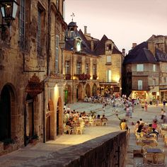 people are sitting at tables in the middle of an old town square with stone buildings and cobblestone streets