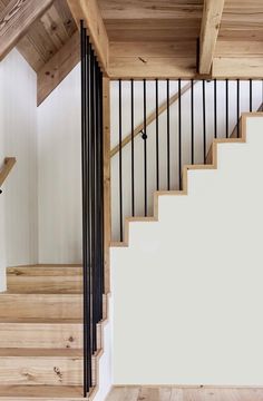 a wooden stair case next to a white wall with black railings and wood flooring