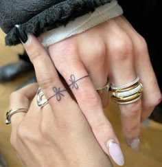 two people with matching rings on their fingers holding each other's hands and one has a flower tattoo on the middle finger