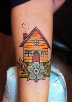 a woman's arm with a small house tattoo on her left forearm and an orange flower in the center